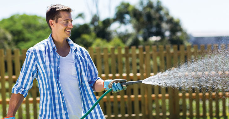 A man smiles while spraying a house at a house